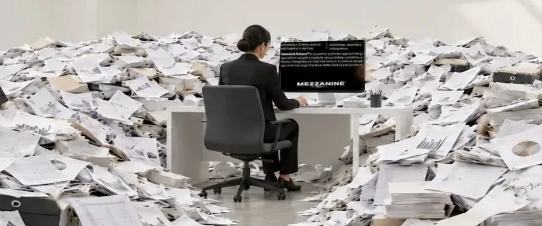 Drowning in documents: a woman works at the Mezzanine screen, surrounded by mountains of paper