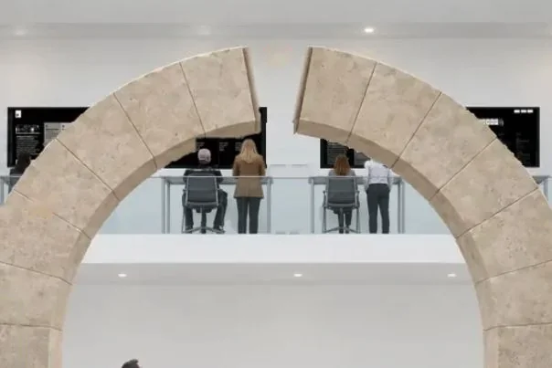 Through a stone arch, the Mezzanine balcony: people at a row of live screens above the gallery floor